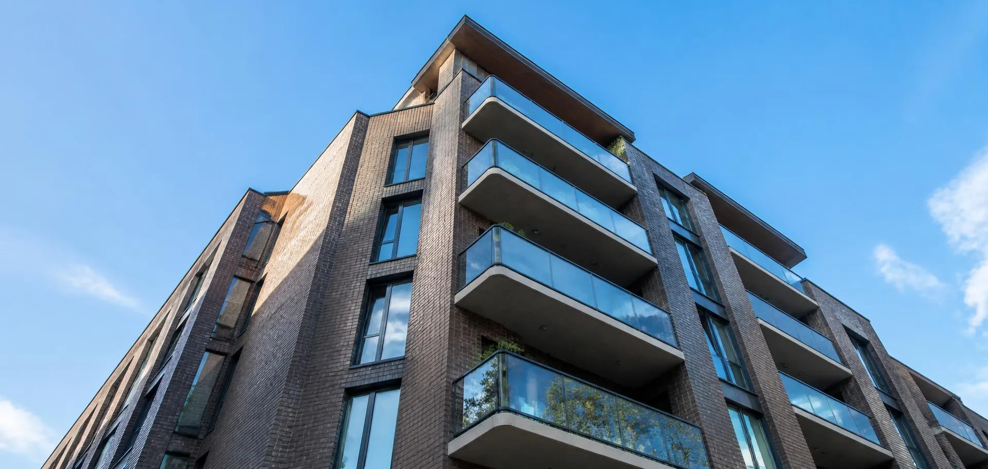 Modern brick and glass apartment building photographed looking steeply upward against a blue sky